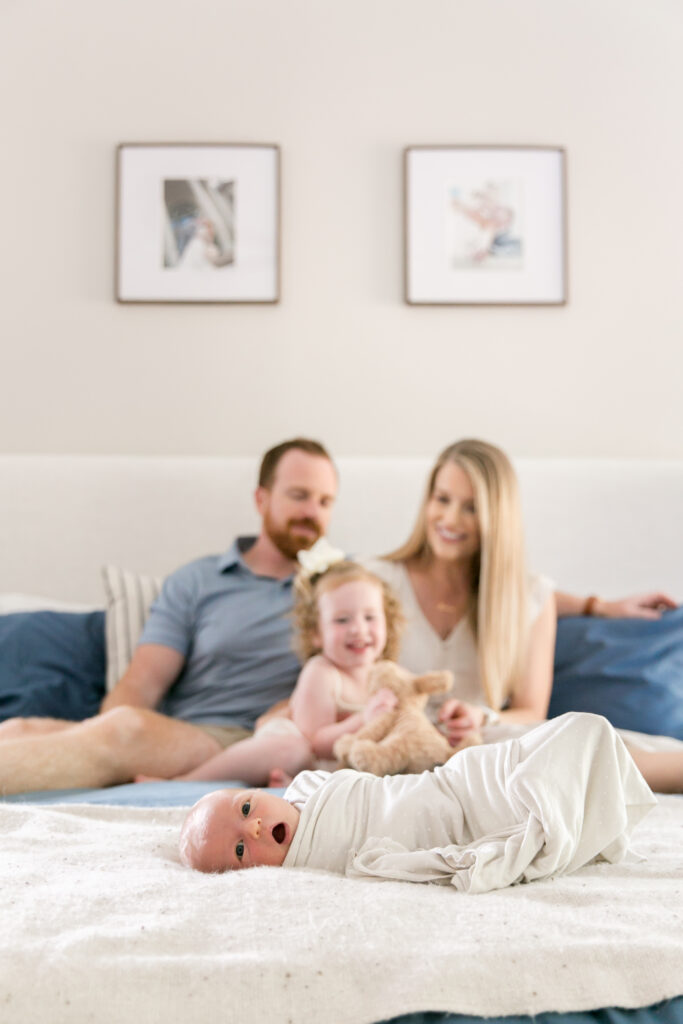 big sister sitting with parents on bed behind newborn during family newborn photo session in Columbia SC