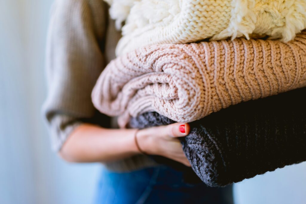 A person holds folded knit blankets, representing decluttering and organizing as you prepare for your newborn.