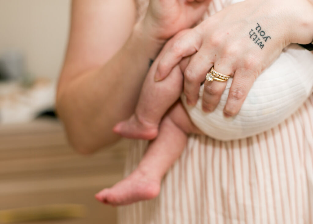 Close up of mom's hand with the words "with you" tattooed on it holding a baby at her Columbia, SC newborn photo session