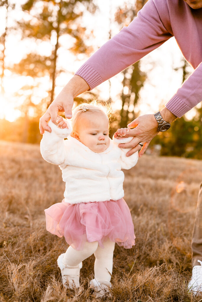 Toddler girl in pink tutu walking in golden field during outdoor family photo session in Columbia SC.