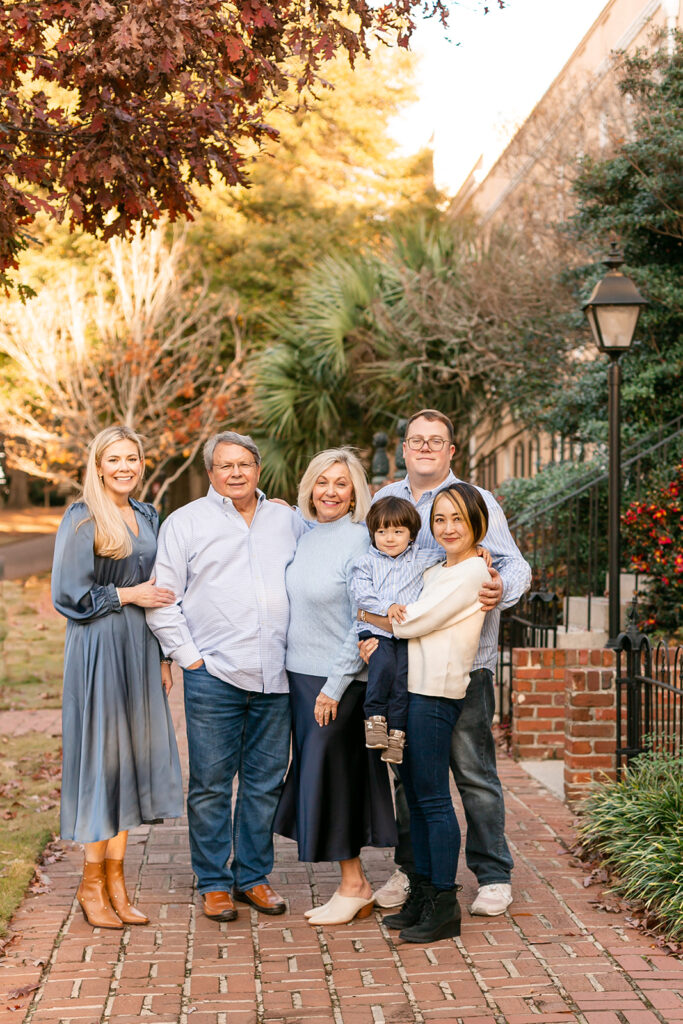 Extended family portrait in Columbia SC with grandparents, parents, and children posing on brick path lined with trees.