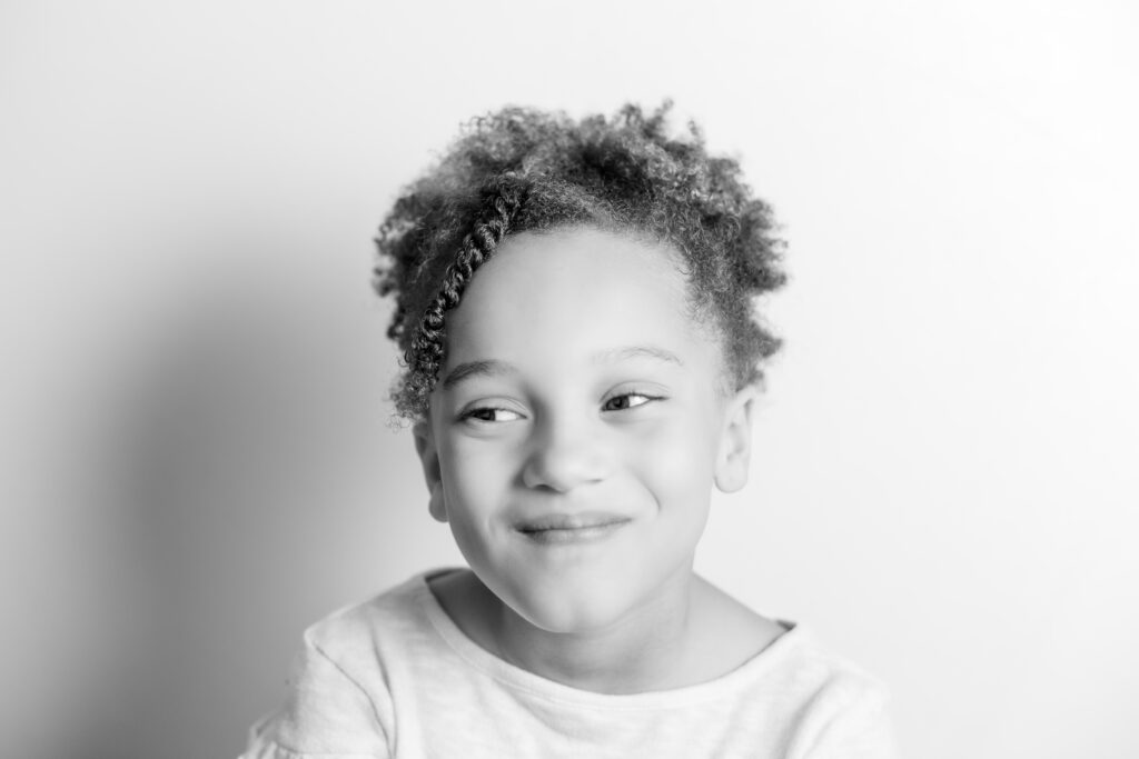 Black and white portrait of a child laughing with an open mouth, capturing a joyful moment in a studio session