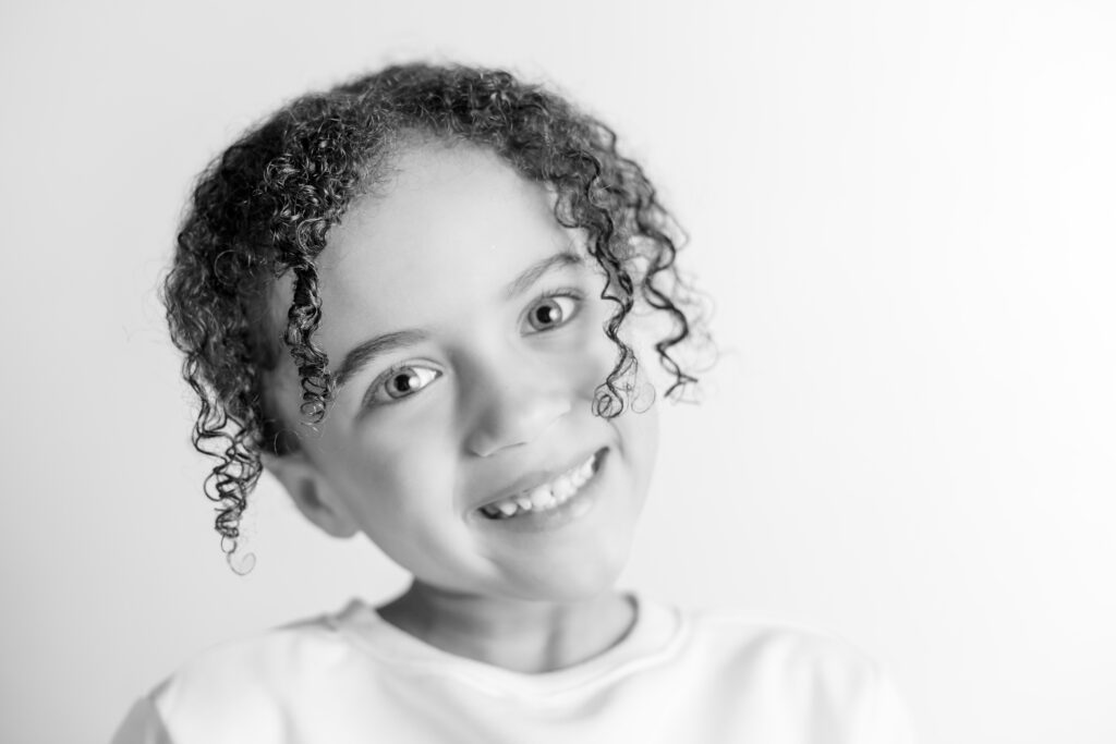 Black and white portrait of a young girl smiling with a head tilt, capturing personality in a Columbia South Carolina studio